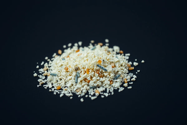 Small pile of irregular pale and muted-color fragments photographed at a low angle on a dark surface.