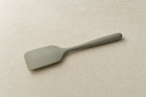 Muted sage silicone spatula with a small split along one edge on a pale stone surface.
